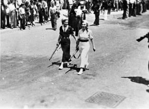 Dues noies armades acompanyant les primeres columnes de combatents que marxen cap al front d'Aragó, a Barcelona