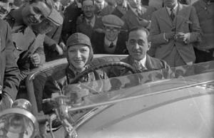 Un pilot dins el seu automòbil, acompanyat del seu copilot i envoltats de ciutadans, a una cursa